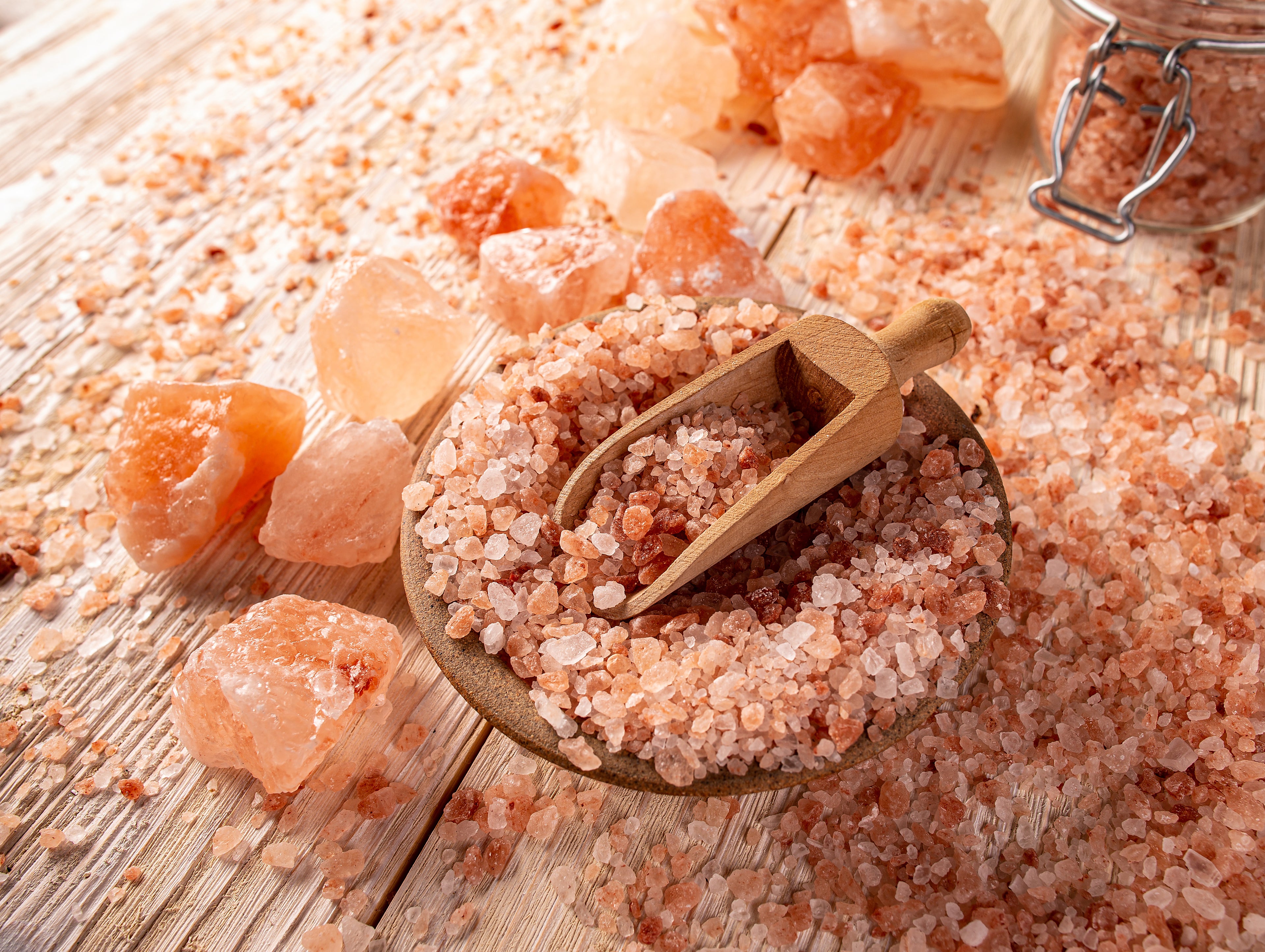 Pink himalayan salt with a wooden scoop on a wooden surface